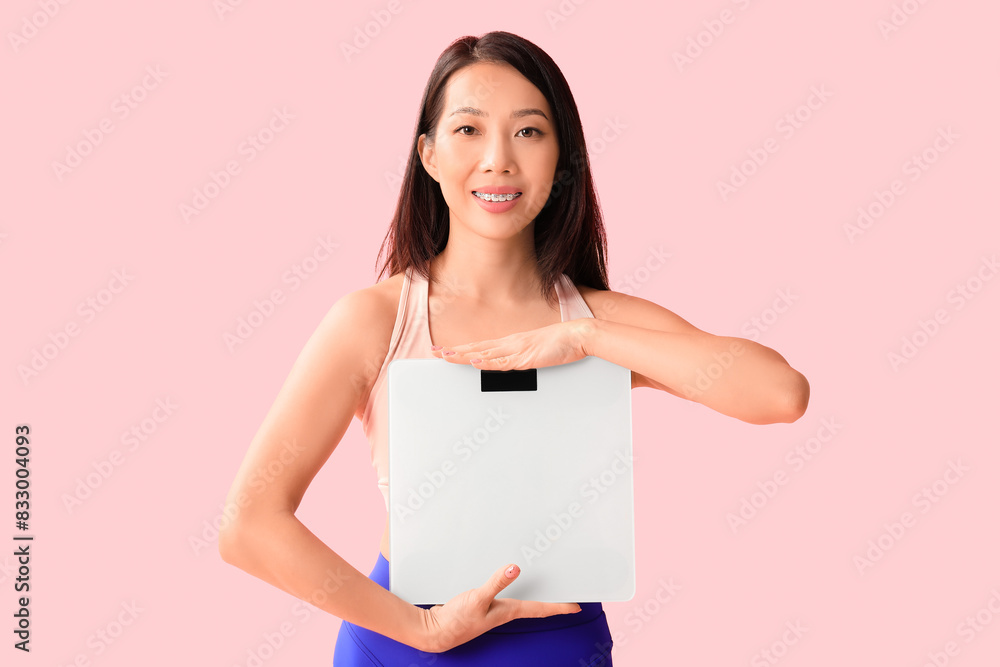 Beautiful young Asian woman with scales on pink background. Weight loss concept