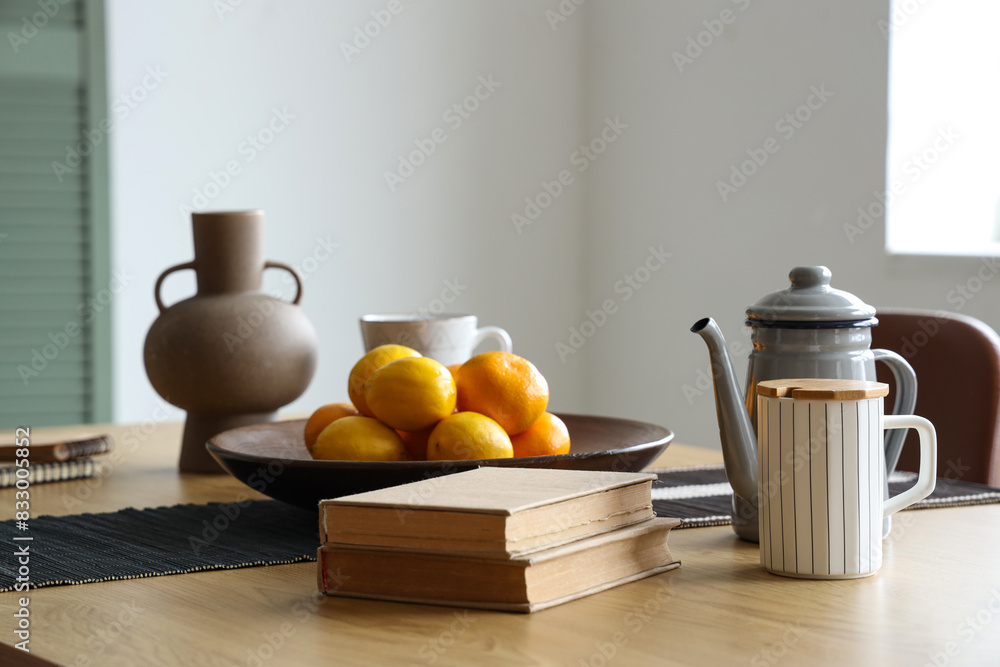 Citruses with teapot, books and vase on dining table in room