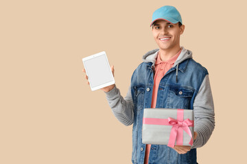 Male courier with gift box and tablet computer on beige background