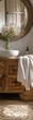 © Mind - Rustic bathroom decor with a wooden vanity, round mirror, white towel, and flowers in a vase creating a cozy, natural ambiance.