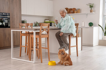 Canvas Print - Senior woman with glass of water and Pomeranian dog in kitchen