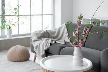 Poster - Stylish interior of living room with sofa and coffee table with blooming branches