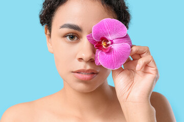 Poster - Beautiful young African-American woman with purple orchid flower on blue background