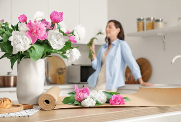 Poster - Beautiful young woman decorating bouquet of peony flowers in kitchen