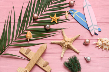 Sticker - Wooden airplane, starfish, toy surfboard and palm branch with Christmas balls on pink wooden background. Top view