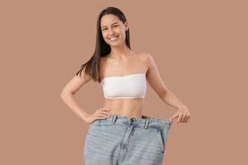 Sticker - Beautiful young happy woman in loose jeans on brown background. Weight loss concept