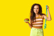 © Pixel-Shot - Happy young African-American woman with burger and measuring tape on yellow background. Diet concept