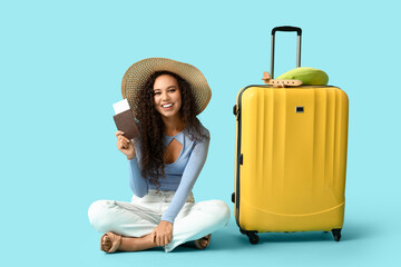 Wall Mural - Happy young African-American woman with suitcase, passport and ticket sitting on blue background