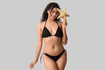 Sticker - Beautiful young African-American woman in stylish black swimsuit with starfish on grey background