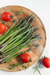 Sticker - Fresh Asparagus and Tomatoes on a Wooden Cutting Board Against a White Background