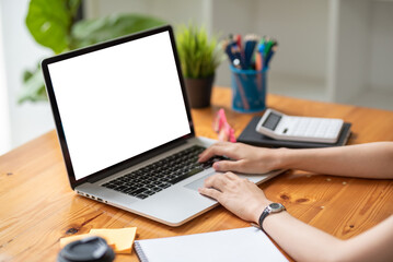 Person working on a laptop with a blank screen at a wooden desk, surrounded by office supplies and a calculator.