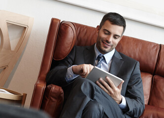 Wall Mural - Reading, tablet and corporate man on couch for online, research and smile in waiting room. Trader, stock market and internet with technology for planning and proposal for business meeting in New York