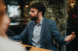 © qunica.com - A young bearded man dressed in smart casual attire engaging in a business conversation over coffee.