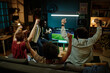 © AnnaStills - Rear view of four young male friends enjoying watching soccer match on TV late in evening