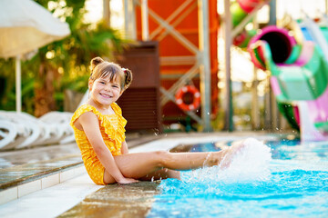 Little preschool girl playing in outdoor swimming pool by sunset. Child learning to swim in outdoor pool, splashing with water, laughing having fun. Family vacations. Healthy children sport activity