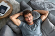© AspctStyle - Smiling man relaxing on couch with hands behind head, enjoying a peaceful moment at home in a cozy living room