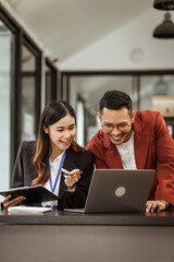 Middle-aged businessman and young Asian businesswoman diligently working at desks, managing tasks as recruitment, training, performance management, inclusive organizational culture.