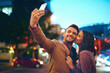 © Adene Sanchez/peopleimages.com - Couple, selfie and city with love at night with smartphone, outside and honeymoon for marriage. Relationship, celebration and profile picture for social media with smile or hugging in New York.