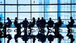 © Felippe Lopes - Silhouetted business professionals engaged in a meeting in a modern office with large blue-tinted windows, reflecting a collaborative and corporate atmosphere.