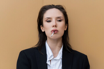 Attractive caucasian young woman in suit smoking cigarette, posing while walking outdoors on spring day. Sexy, stylish and elegant lady. Fashion, Lifestyle.