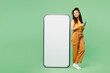 © ViDi Studio - Full body young woman wear yellow tank shirt top big huge blank screen mobile cell phone with workspace copy space mockup area using smartphone isolated on plain green background. Lifestyle concept.