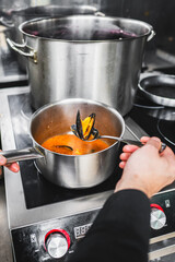 Poster - Close-up of hands preparing food in stainless steel pots on a modern stove, showcasing domestic cooking.