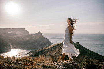 Wall Mural - A woman in a white dress stands on a hill overlooking the ocean. The scene is serene and peaceful, with the woman's dress billowing in the wind. The combination of the ocean.