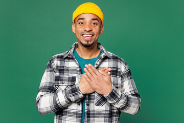 Wall Mural - Young grateful smiling happy man of African American ethnicity he wears shirt blue t-shirt yellow hat put folded hands on heart isolated on plain green background studio portrait. Lifestyle concept.