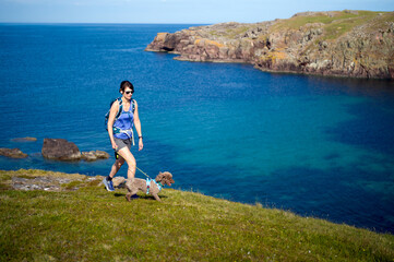 Canvas Print - A female hiker and their dog out for a coastal walk near Reiff above the turquoise blue water of Camas Eilean Ghlais in the Scottish Highlands in the UK.