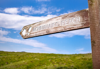 Poster - A wooden signpost giving directions to the sandy beach of Achnahaird Bay in the Scottish Highlands on a warm sunny summers day in the UK.