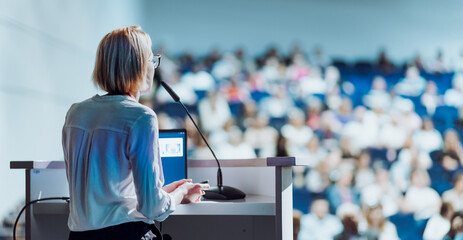 Female speaker giving a talk on corporate business conference. Unrecognizable people in audience at conference hall. Business and Entrepreneurship event