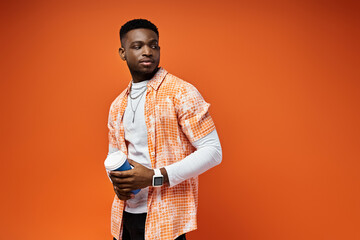 Wall Mural - A fashionable young African American man in an orange shirt stands confidently against a matching orange background.