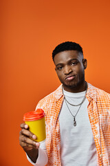 Wall Mural - Young man holding coffee cup against vivid orange backdrop.