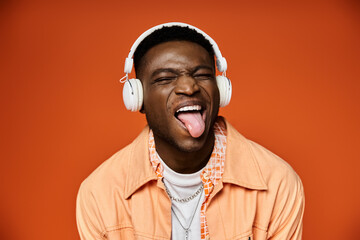 Wall Mural - Stylish young African American man with headphones sticking out his tongue.