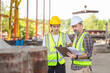 © JU.STOCKER - Senior engineer and female foreman team checking project at precast concrete factory site, Caucasian engineer and worker in hardhats discussing on construction site