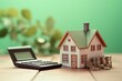 © tohceenilas - Miniature house model, calculator, and coins on a wooden table, symbolizing home finances, mortgage, and investment with a green background.