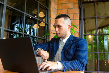 Male businessman working on laptop conferencing with the customer checking the time on his watch. the background being a brick wall,