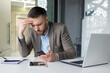 © Liubomir - A stressed businessman in a modern office receiving bad news on his phone, looking worried and frustrated.