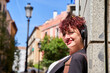 © Oscar - A woman with red hair and a black jacket is wearing headphones and smiling. She is standing in front of a building