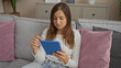 © Krakenimages.com - Young attractive caucasian woman sitting in a living room using a tablet, seamlessly blending into the cozy home interior.