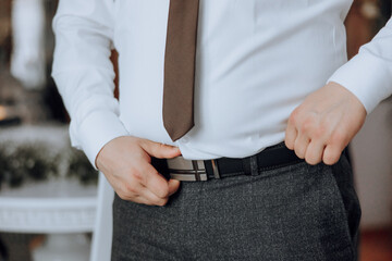 Wall Mural - A man in a white shirt and a brown tie is adjusting his pants. Concept of formality and attention to detail, as the man takes care to ensure his outfit is properly fitted