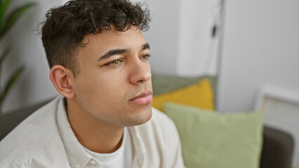 Wall Mural - A thoughtful young man with curly hair rests at home, showcasing contemplation and casual style.