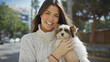 © Krakenimages.com - A young hispanic woman hugs her terrier on a sunny city street, posing with a smile for a heartwarming urban scene.