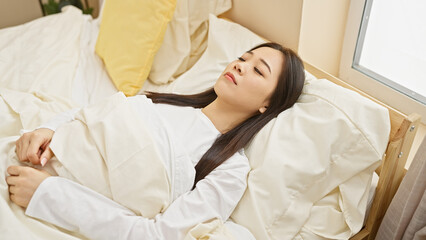 Canvas Print - A young asian woman lies in bed, seemingly asleep, in a well-lit bedroom, embodying tranquility and rest.