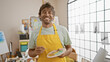 © Krakenimages.com - A cheerful man with green eyes and a beard wearing a yellow apron holds a paintbrush and palette in an art studio.