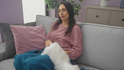 Wall Mural - A serene woman relaxes on a sofa with her fluffy bichon maltese in a cozy, modern living room.