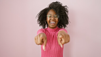 Wall Mural - A cheerful black woman pointing at the camera and smiling indoors against a plain background.