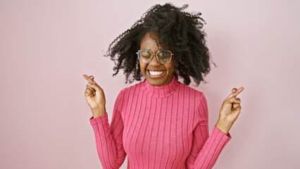 Wall Mural - A cheerful black woman with glasses smiles while crossing her fingers in an indoor pink setting.