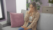 © Krakenimages.com - A young blonde woman in a living room holds her nose due to a bad smell, sitting on a sofa with pink and gray pillows and a plant in the background.