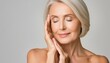 © Marko - gorgeous senior older woman with closed eyes touching her perfect face skin, beautiful portrait mid 50s aged woman, facial antiage lift skin care products, isolated on light grey background